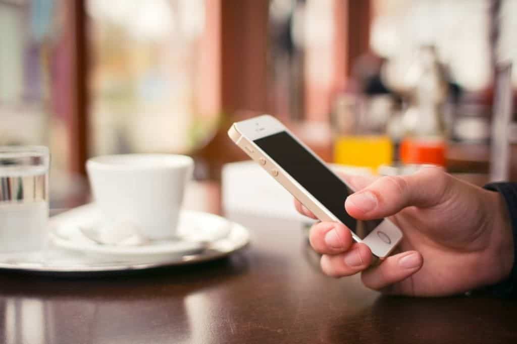 Gambar Tangan Pegang HP Ponsel Smartphone Di Atas Meja Cangkir Gelas Putih